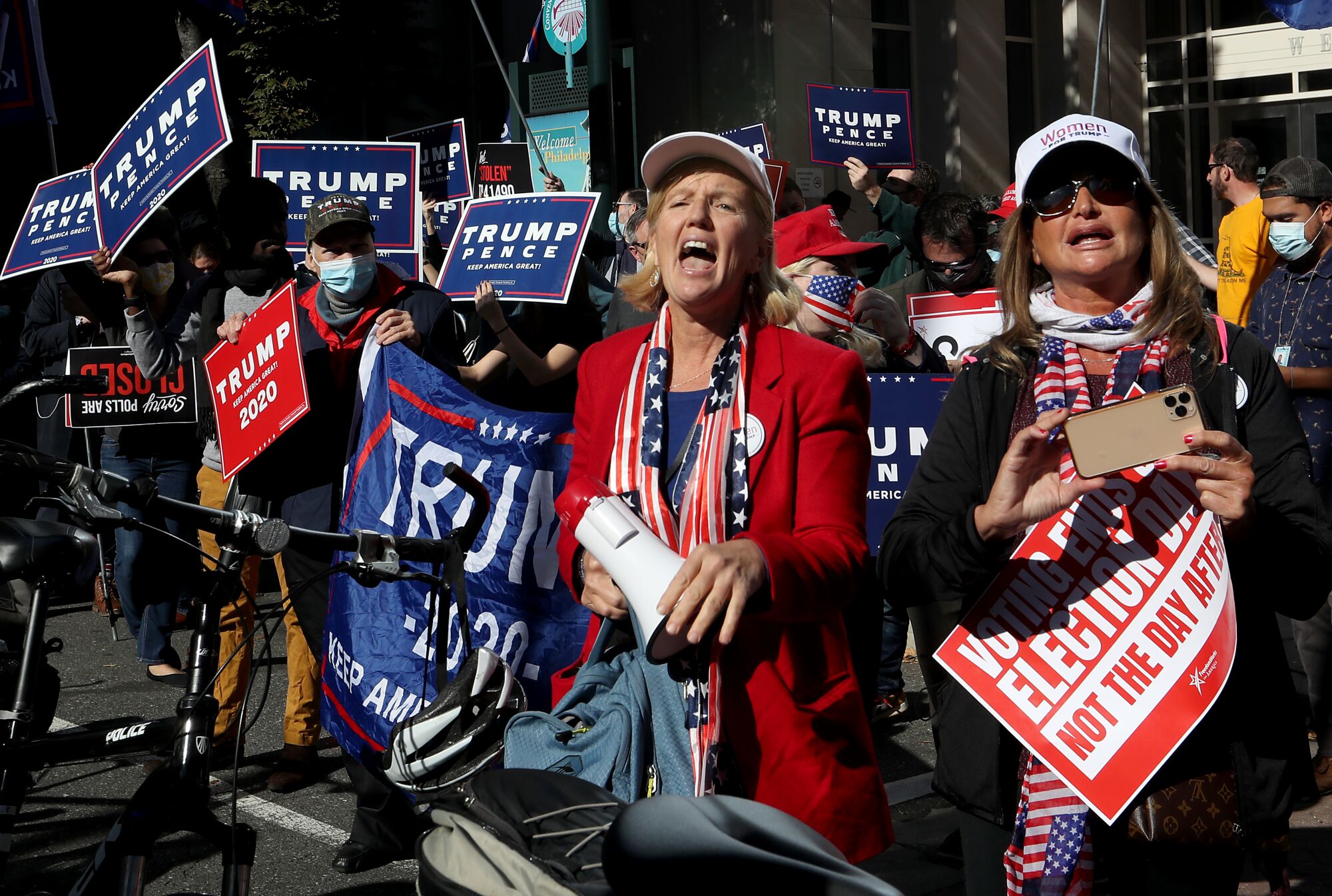 People hold signs reading "Trump 2020," "Trump Pence" and "Voting ends on election day, not the day after."
