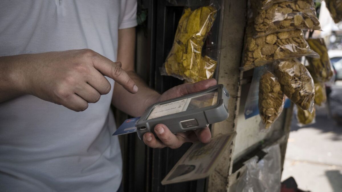 A street vendor uses a portable cash reader to sell a chocolate bar at a kiosk in Caracas.