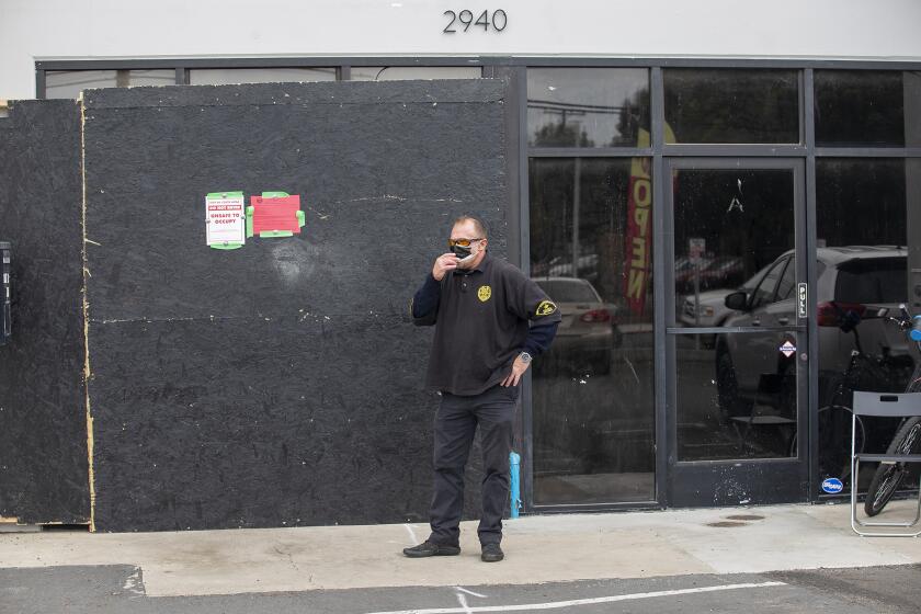 Robbie Burke, with MPP Security and Bodyguards, stands outside of an illegal dispensary at 2940 College Ave. in Costa Mesa that was raided Tuesday morning by the Bureau of Cannabis Control with assistance from the Costa Mesa Police Department.