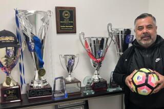 Carlos Marroquin stands next to trophies and awards won by the Santa Clarita Blue Heat.
