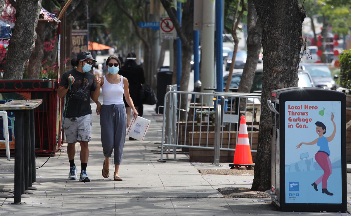 A man and a woman, both wearing masks, walk along Santa Monica Blvd. in West Hollywood.