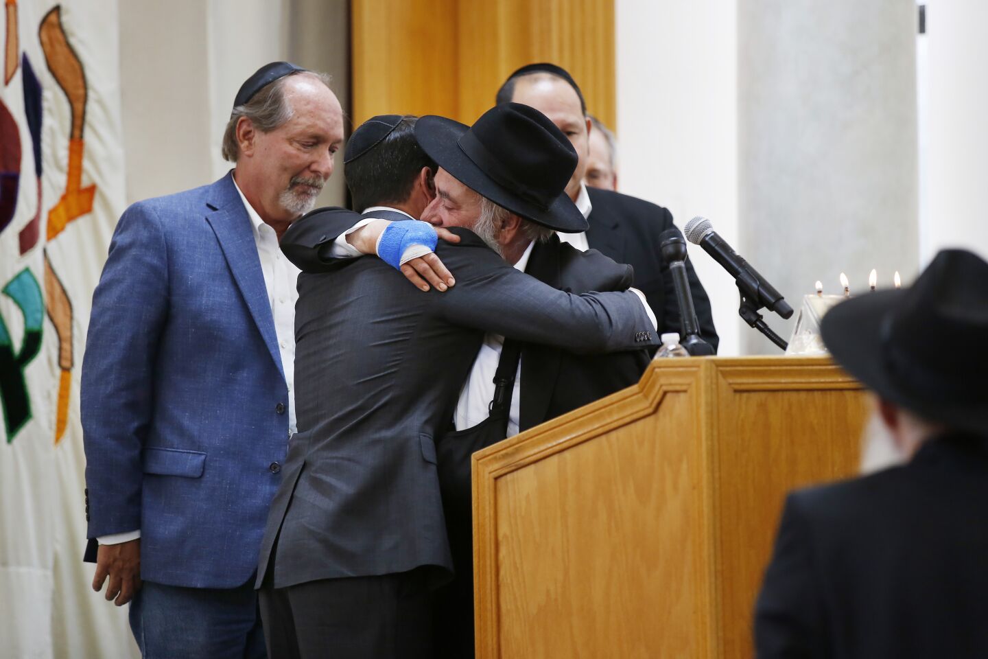 Oscar Stewart, left, who was called a hero in the Poway shooting, is hugged by Rabbi Yisroel Goldstein as Poway Mayor Steve Vaus, left, looks on during a service for Lori Gilbert-Kaye, 60, at the Chabad of Poway on April 28, 2019 in Poway, California. Gilbert-Kaye was killed by a gunman at the synagogue.