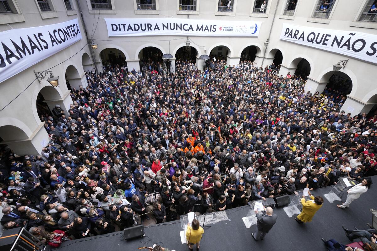 People throng a courtyard to listen to speakers on a podium 