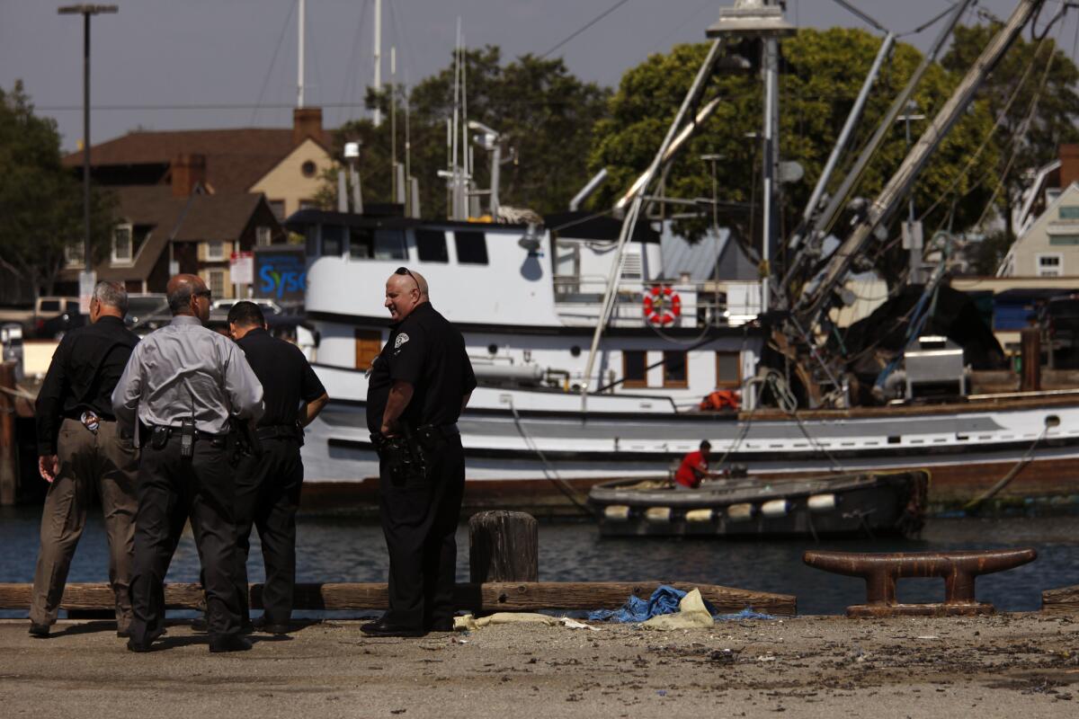 Officers stand near the water's edge at a harbor, with boats in the background.