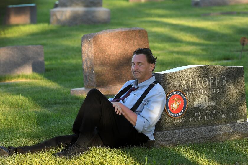 Bill Alkofer leans against his father's tombstone during a visit on Independence Day. Alkofer's father died of a rare neuromuscular disease due to contact with a toxic chemical while serving in the Marine Corps in the 1950s. Alkofer is also dying of a rare neuromuscular ailment.