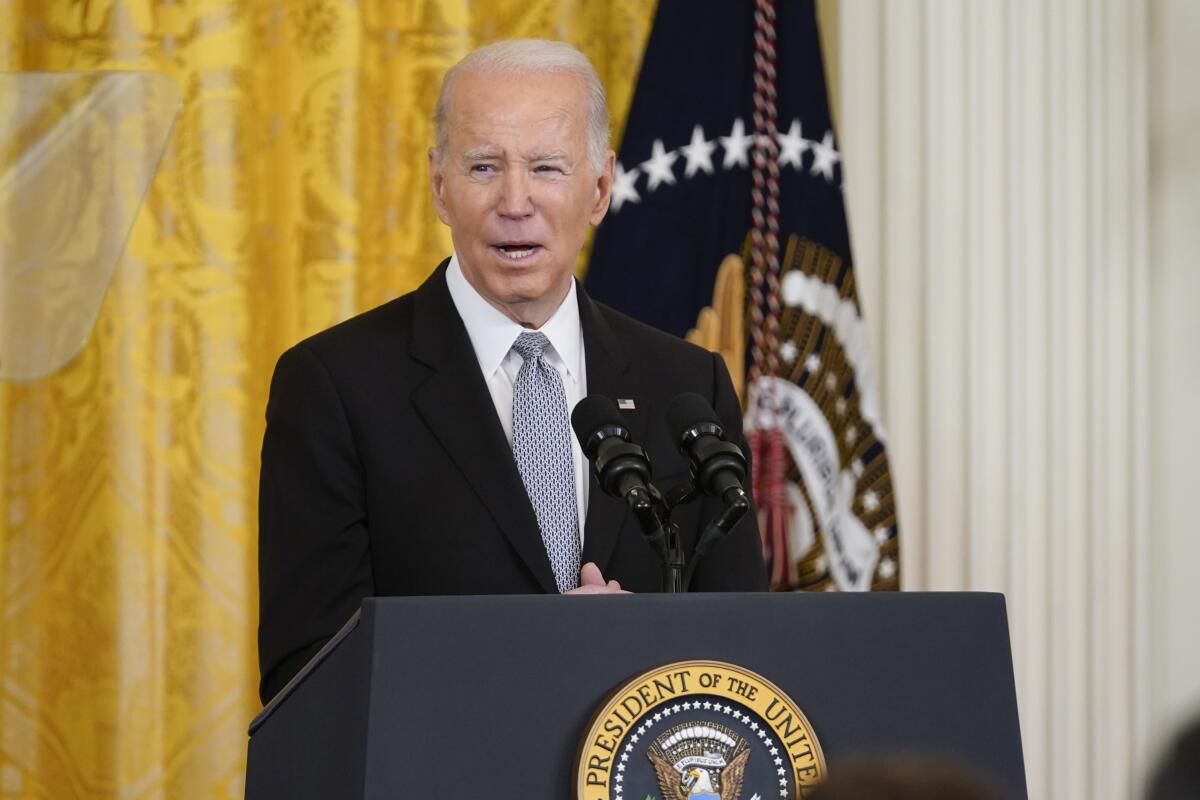 A man with gray hair, in a dark suit and a tie, speaks at a lectern with a presidential seal