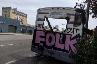 Los Angeles, CA - July 30: Graffiti on the hulking frame of a burned out RV sitting on the 1300 block of W. Washington Blvd. on Sunday, July 30, 2023 in Los Angeles, CA. The RV has been there for three weeks. (Brian van der Brug / Los Angeles Times)