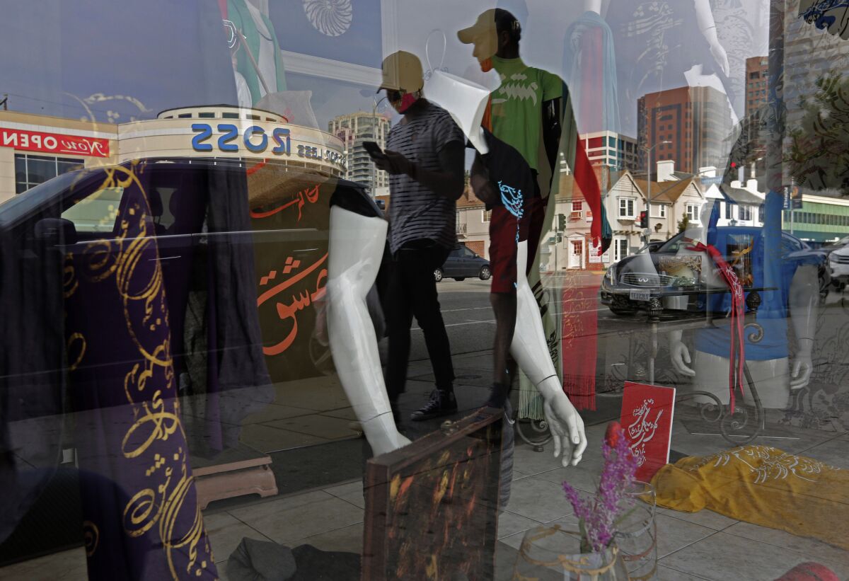 People are reflected in a storefront as they walk down Westwood Boulevard, in Persian Square, in Los Angeles.