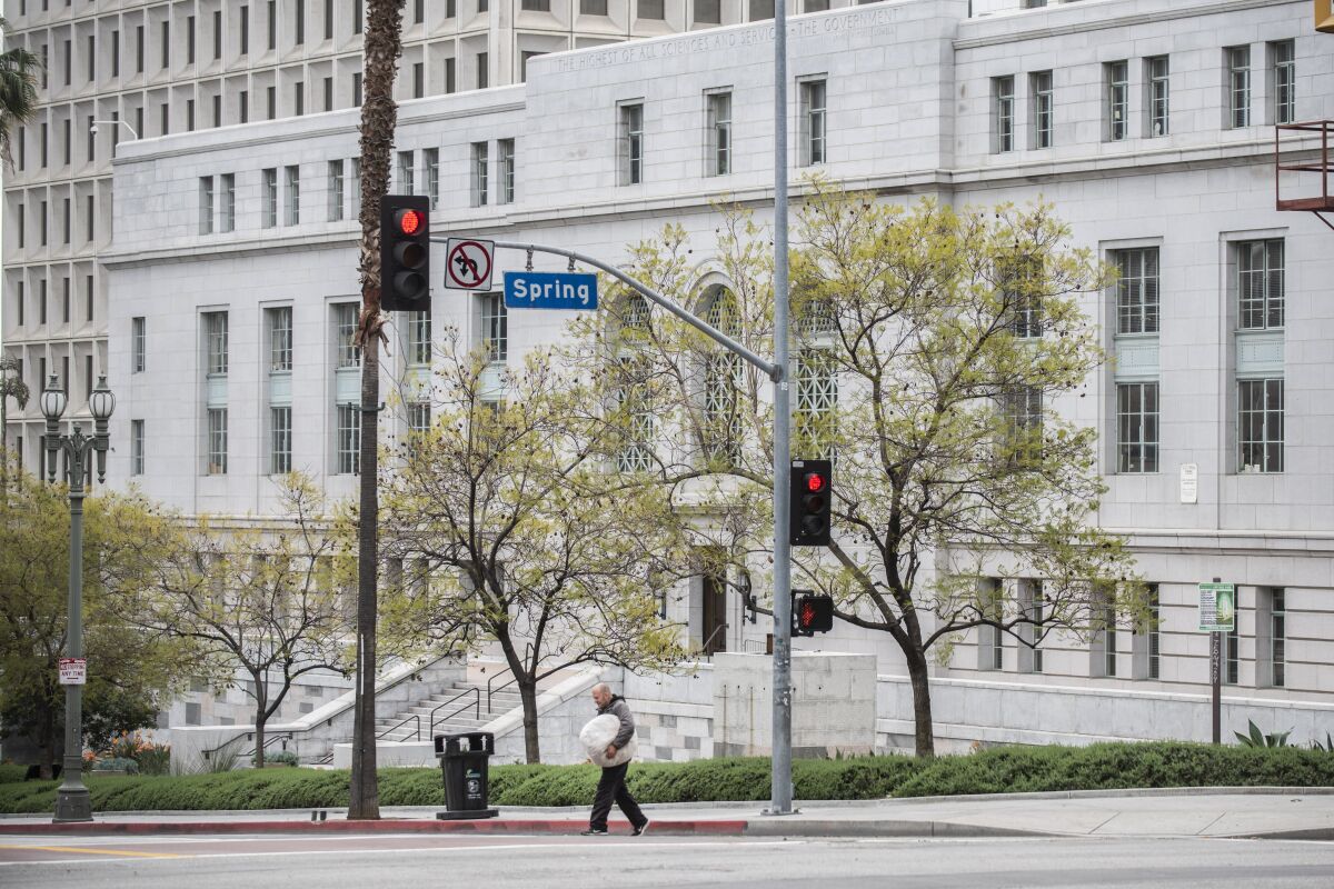 A man crosses the street in front of Los Angeles City Hall