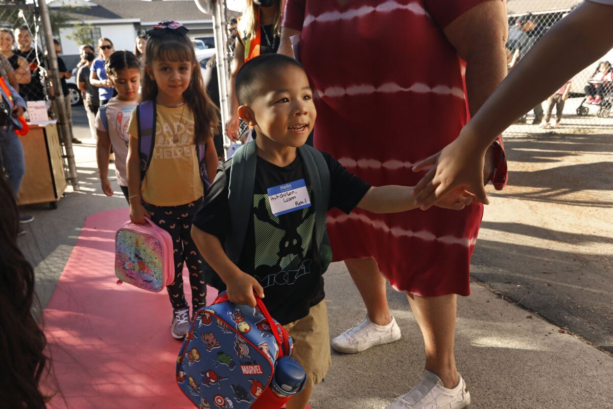 A smiling little boy enters schoolyard gates.