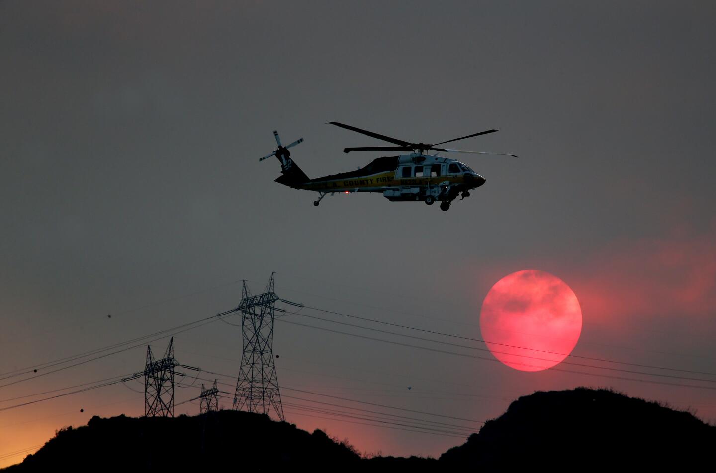 A helicopter flies past a blood-red sun as smoke from the Ranch fire obscures the sky