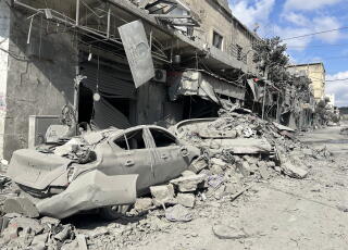 A car lies crushed amid the dusty rubble of a building.