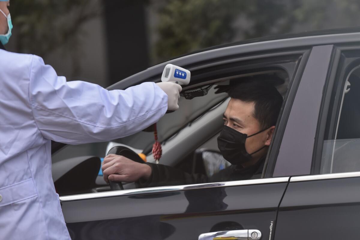 A police takes the temperature of a driver at a checkpoint on a street on the outskirts of Wuhan.