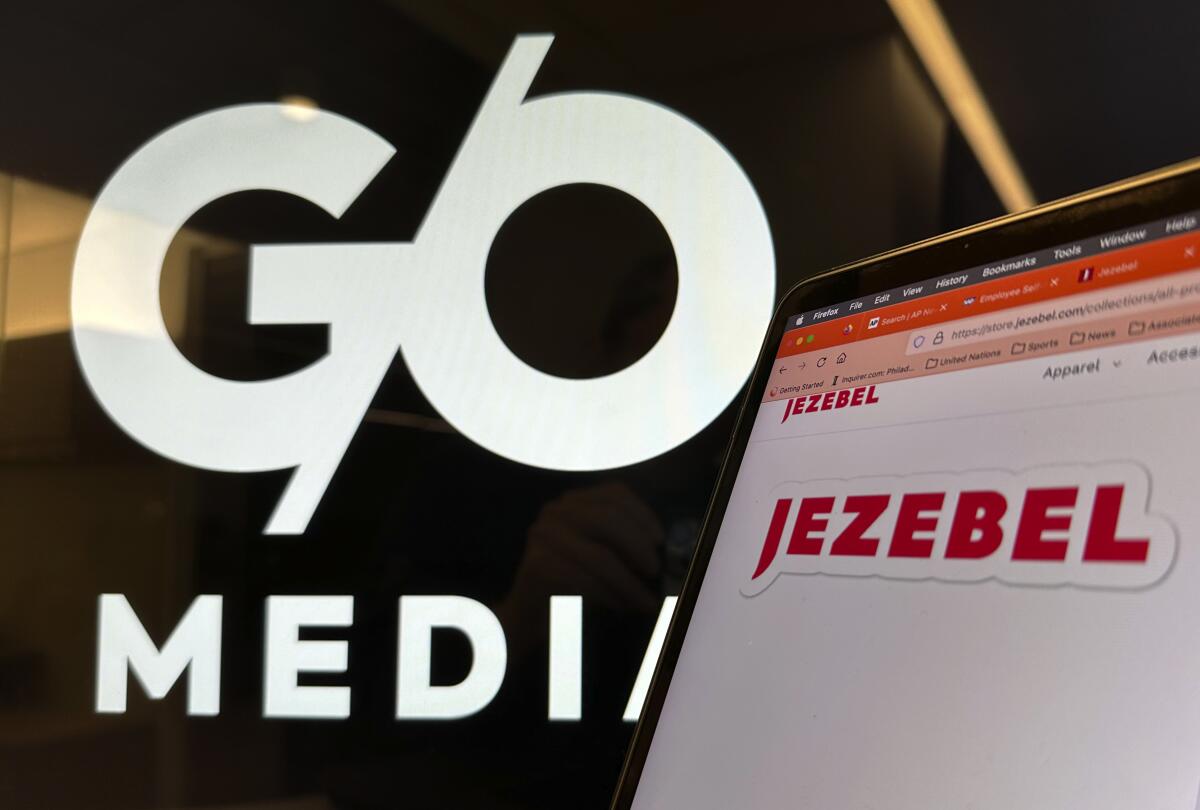 The red-lettered Jezebel logo is displayed on a laptop screen with the black-and-white G/O Media logo behind it