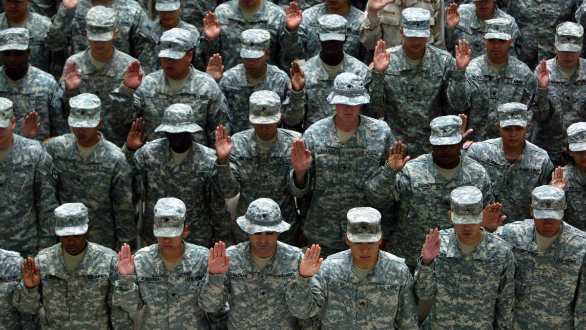U.S. soldiers raise their hands during a naturalization ceremony at Camp Victory in Iraq in 2007. The Pentagon will begin sending a backlog of thousands of green-card holders to recruit training, suspending a Trump administration policy.