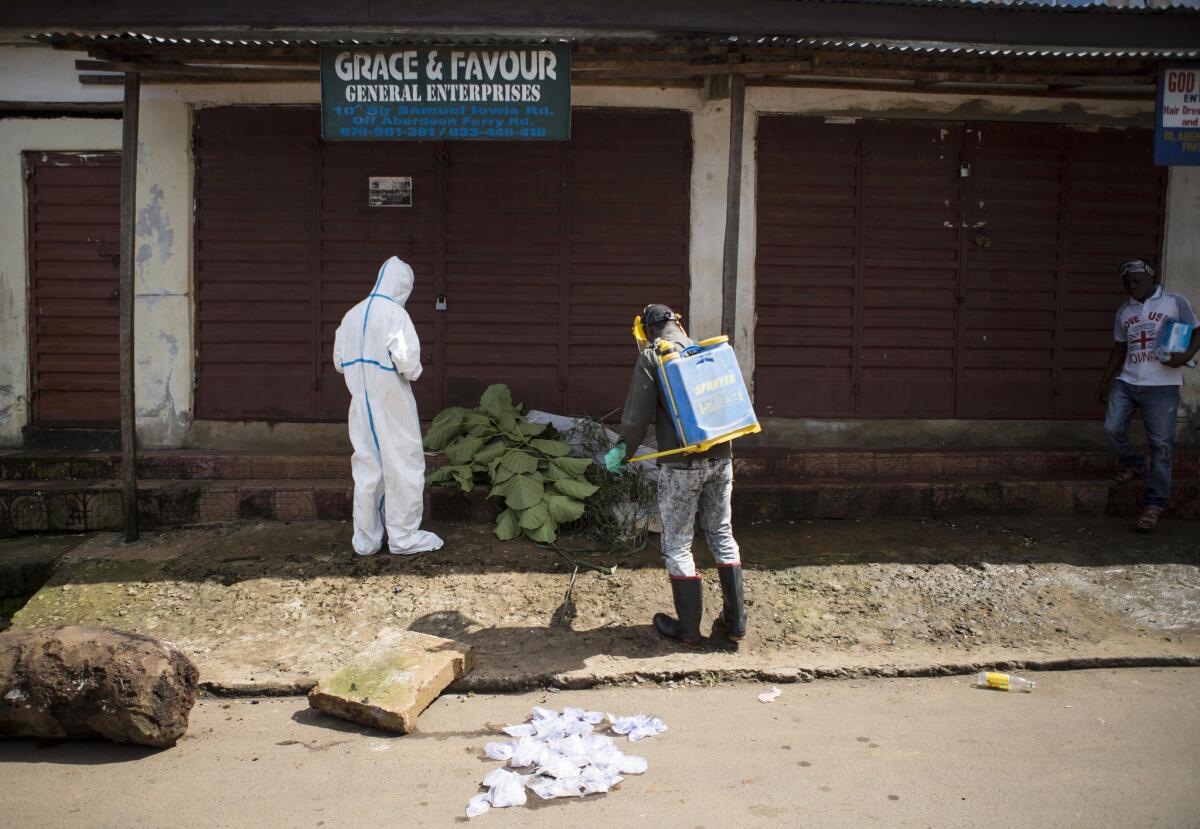 Healthcare workers in Sierra Leone collect samples on Oct. 8 from a person believed to have died of Ebola. The body is covered in leaves.