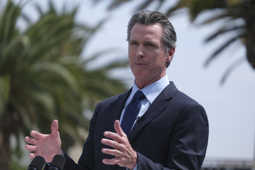 Gov. Gavin Newsom, in a dark suit and tie, gestures with his hands 
