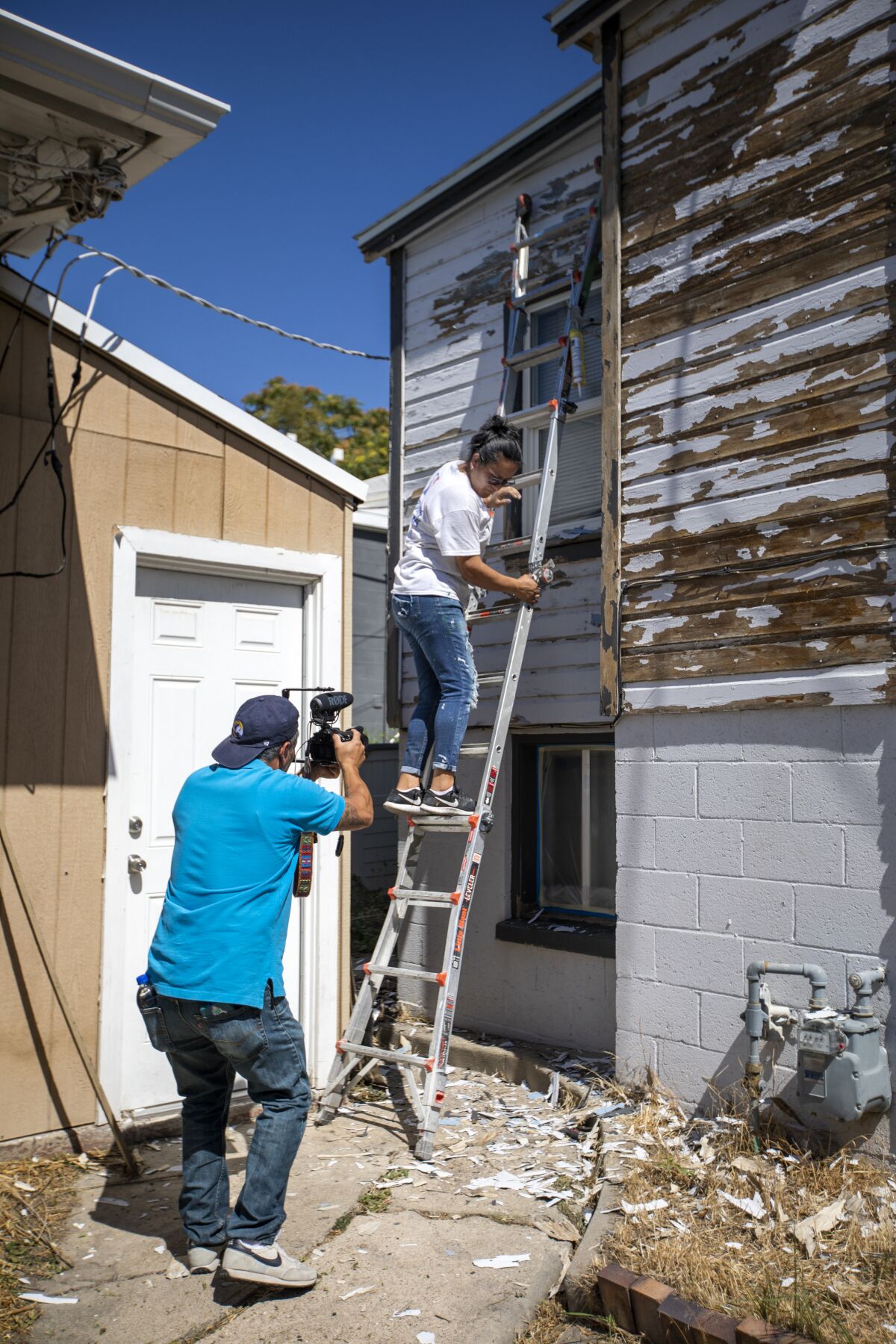 A man in a blue shirt talks to a woman on a ladder.