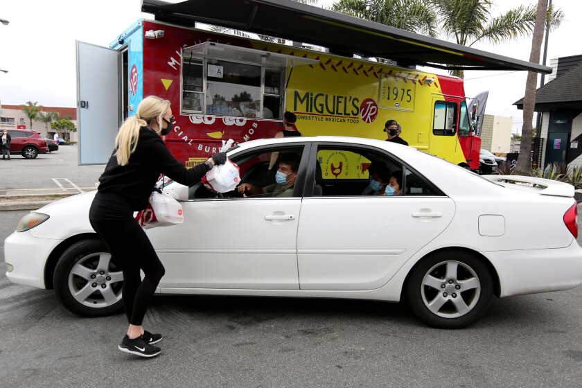 Strut Bar & Club event director Venessa Lynn, left, gives multiple lunches in two bags to Rafael Lopez and his children, of Costa Mesa, during Wednesday's free meals event.