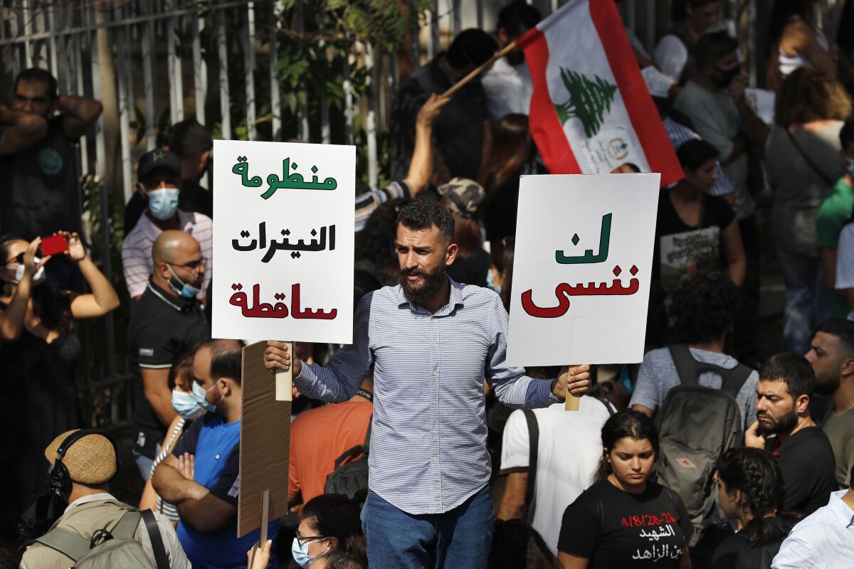 A protester holds Arabic placards that reads: "Will not forget, right, down with the system of nitrates," outside a court building during a demonstration of solidarity with Judge Tarek Bitar who is investigating last year's deadly seaport blast, in Beirut, Lebanon, Wednesday, Sept. 29, 2021. Hundreds of Lebanese, including families of the Beirut port explosion victims, rallied Wednesday outside the court of justice in support of Bitar after he was forced to suspend his work. Bitar is the second judge to take on the complicated investigation. (AP Photo/Hussein Malla)