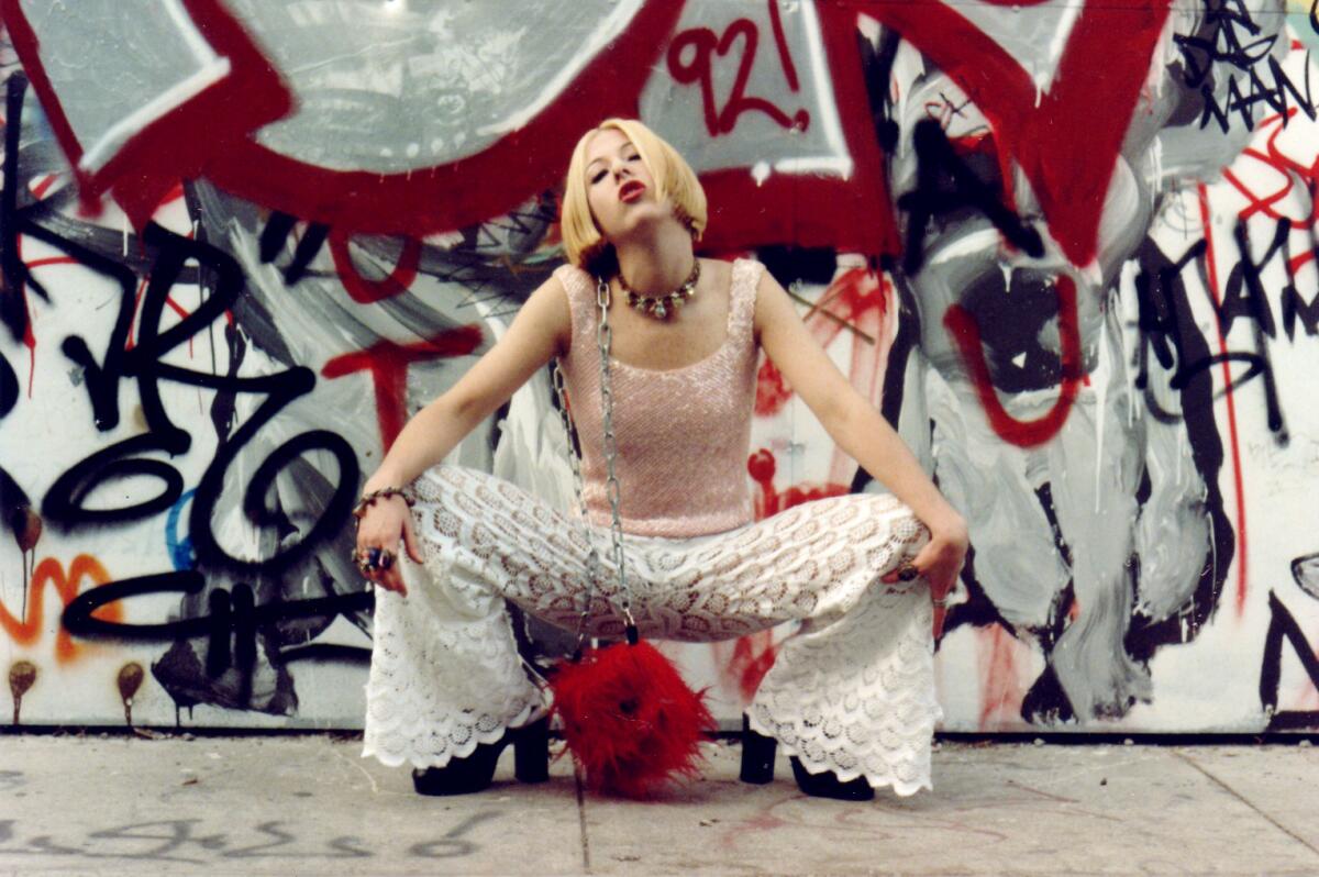 A woman stands in front of a graffiti-strewn wall.