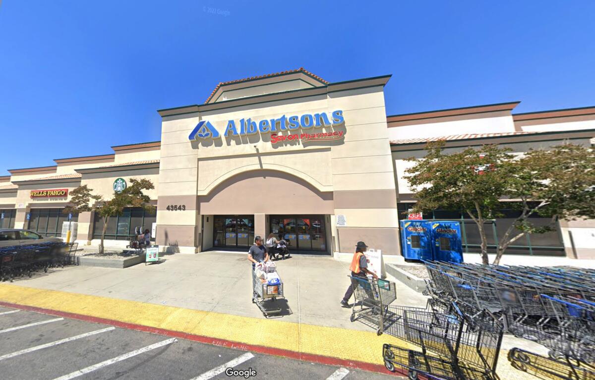 Two people with shopping carts outside the front entrance of an Albertsons grocery store
