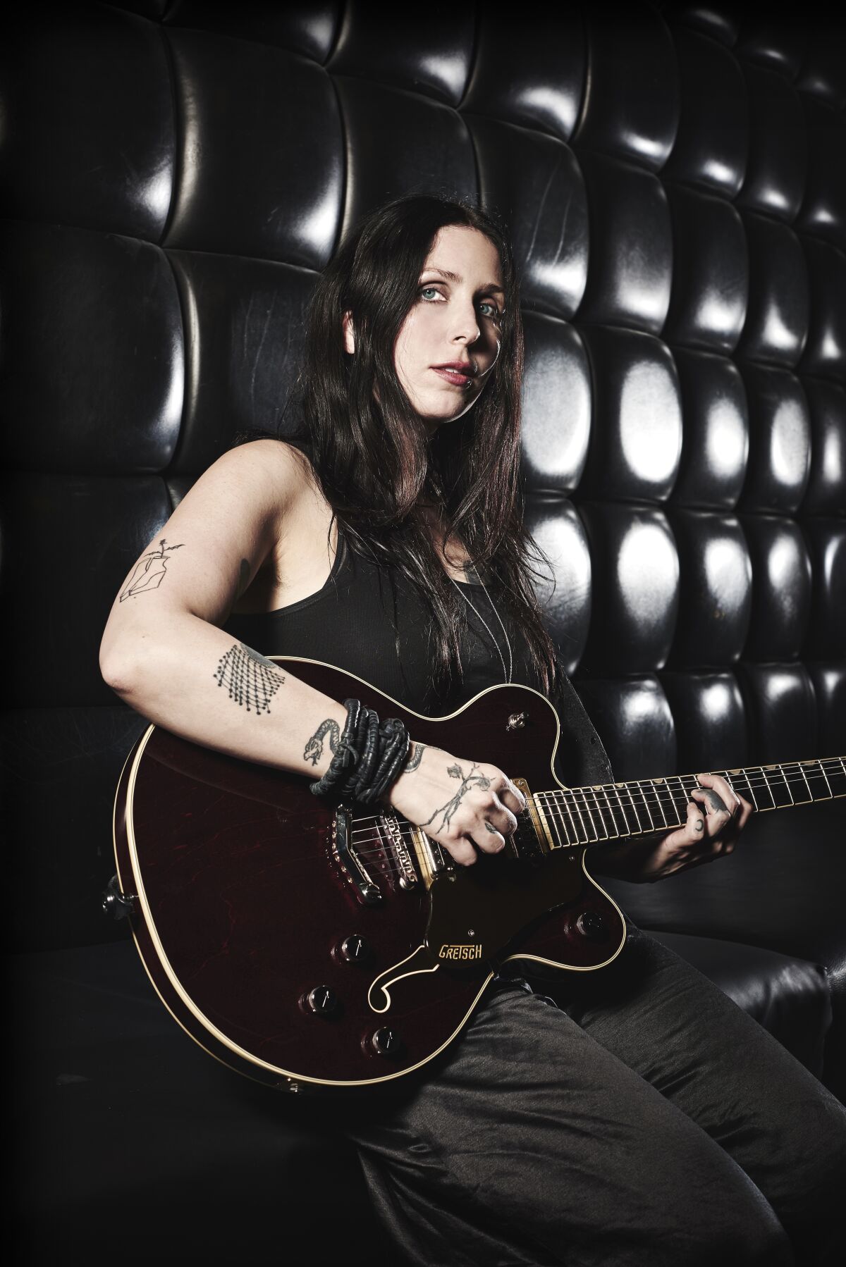 A female musician with tattoos holds a electric guitar.