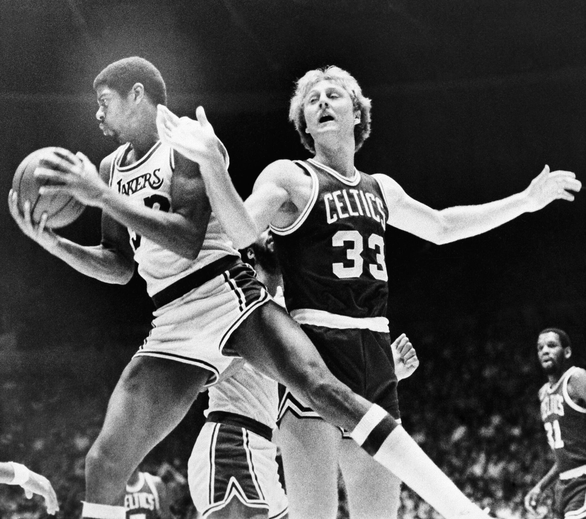 Magic Johnson holds a basketball and turns away from Larry Bird 