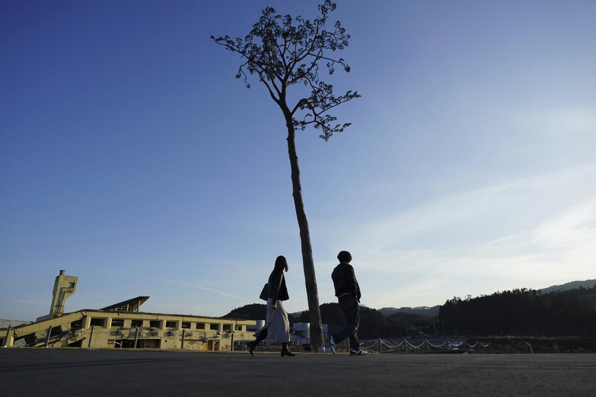 A man and a woman walk near a replica of a lone pine tree that initially survived the 2011 tsunami that flattened the surrounding coastal forest, in Rikuzentakata, Iwate Prefecture, northern Japan, Thursday, March 4, 2021. The tree, which eventually died of seawater exposure, was known as the "Miracle Pine," and townspeople treated, reinforced and then preserved it as a memorial and symbol of hope for the region. (AP Photo/Eugene Hoshiko)