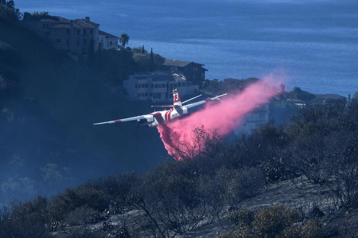FILE - A plane drops retardant on a wildfire near homes Thursday, Feb. 10, 2022, in Laguna Beach, Calif. U.S. officials are testing a new wildfire retardant after two decades of buying millions of gallons annually from one supplier, but watchdogs say the expensive strategy is overly fixated on aerial attacks at the expense of hiring more fire-line digging ground crews. (AP Photo/Ringo H.W. Chiu, File)