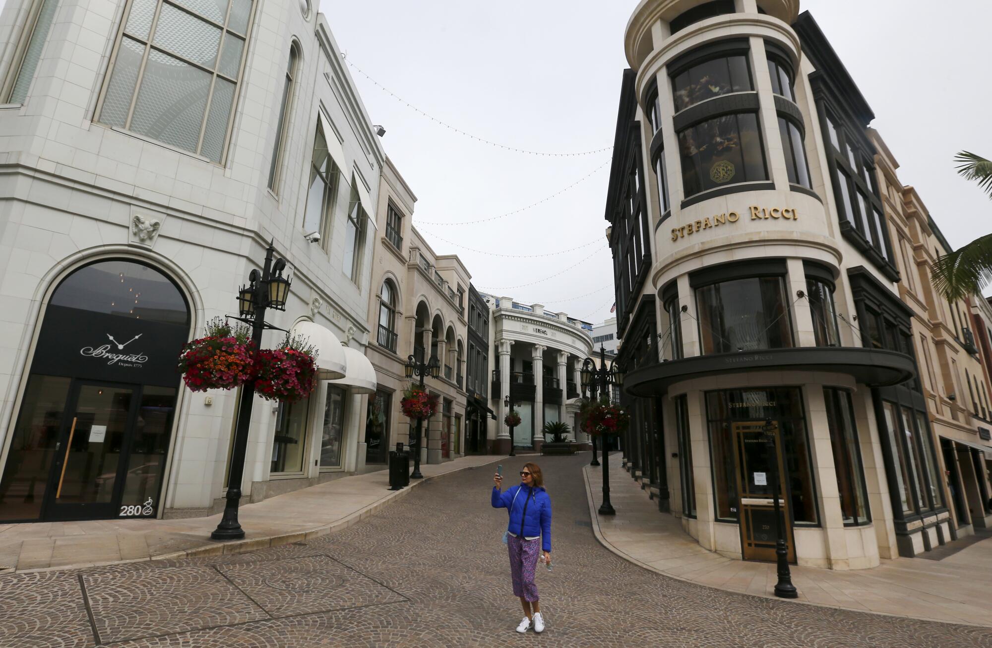 A woman uses a smartphone to record the scene along Rodeo Drive in Beverly Hills, where shops were closed and streets largely devoid of people on March 20.
