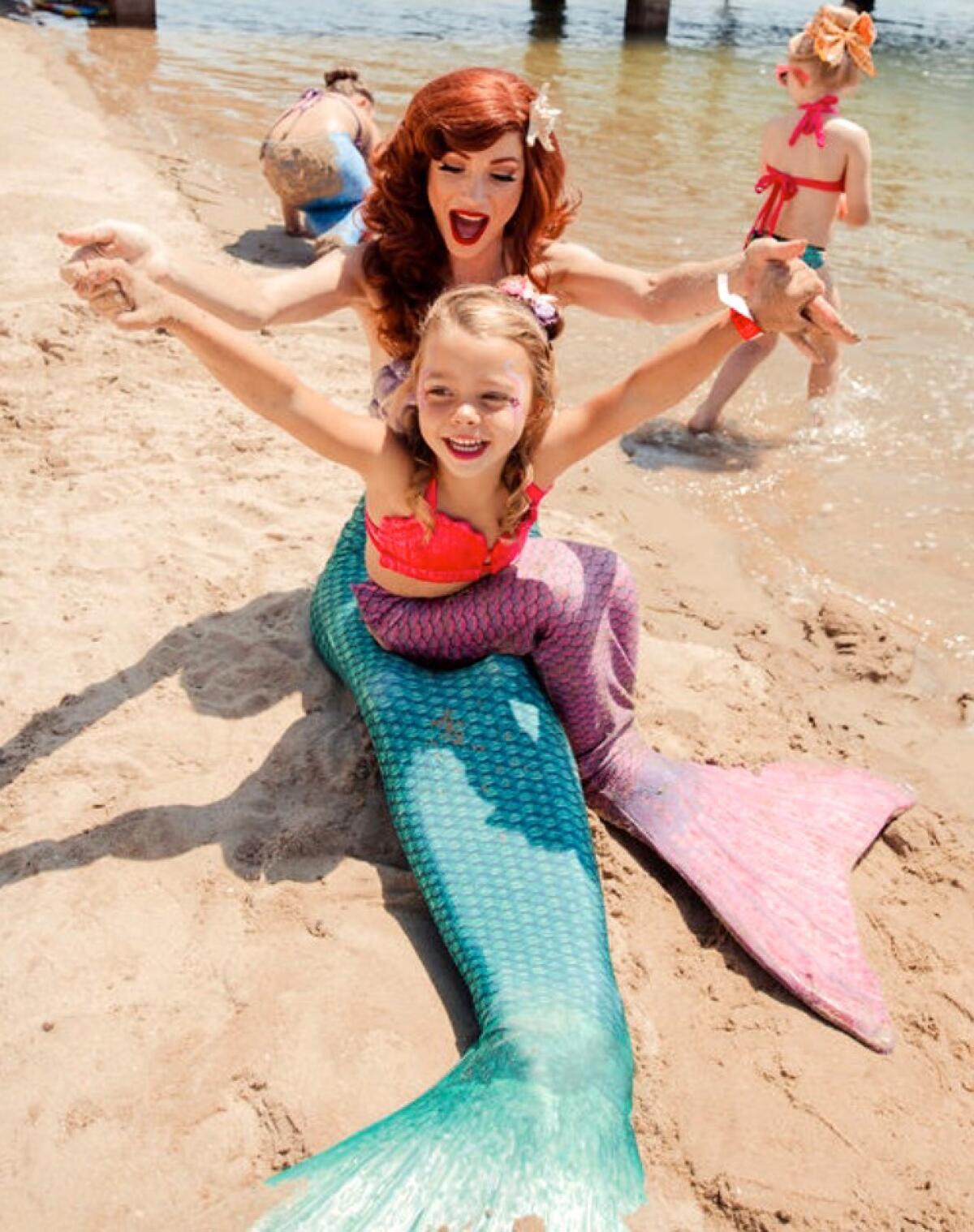 A mermaid from Once Upon An Island entertains a child mermaid on the Balboa Island beach near the business.