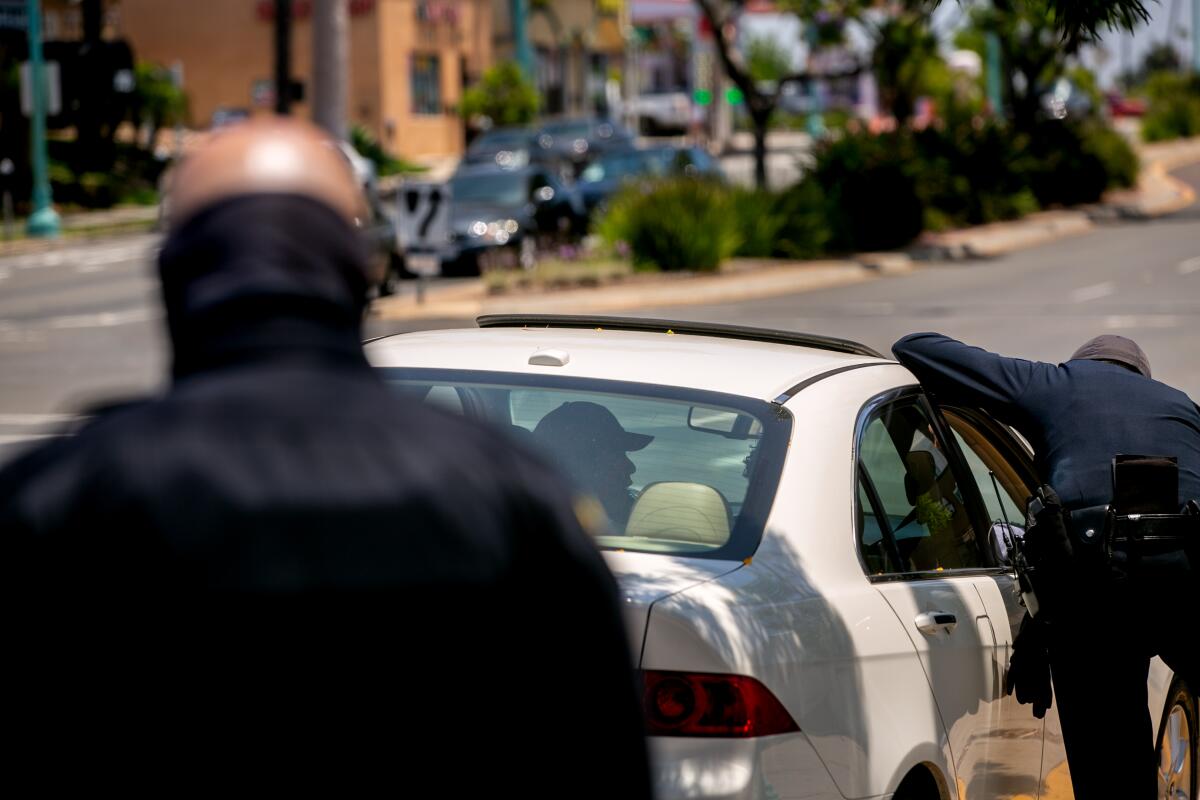 A police officer leans into a white vehicle and speaks to the driver