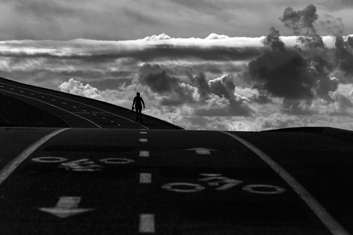 A rollerblader on San Gabriel River Bike Trail silhouetted against cloudy skies over Santa Fe Dam