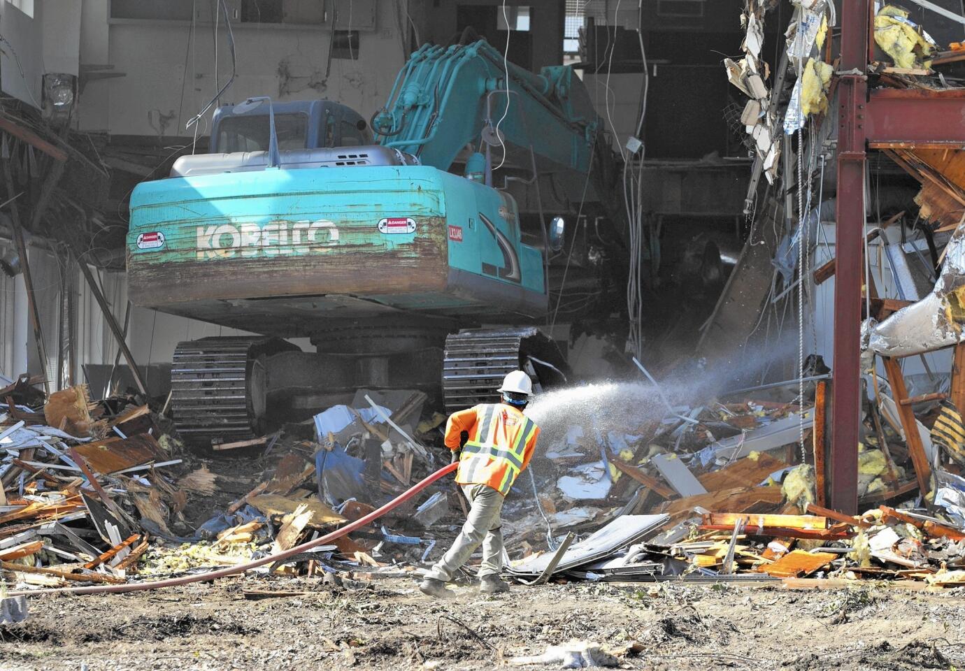 A worker shoots a stream of water into the pile of debris to keep the dust down as he follows an excavator that rips apart one of the old buildings at the former Newport Beach City Hall site, where demolition began Thursday morning.