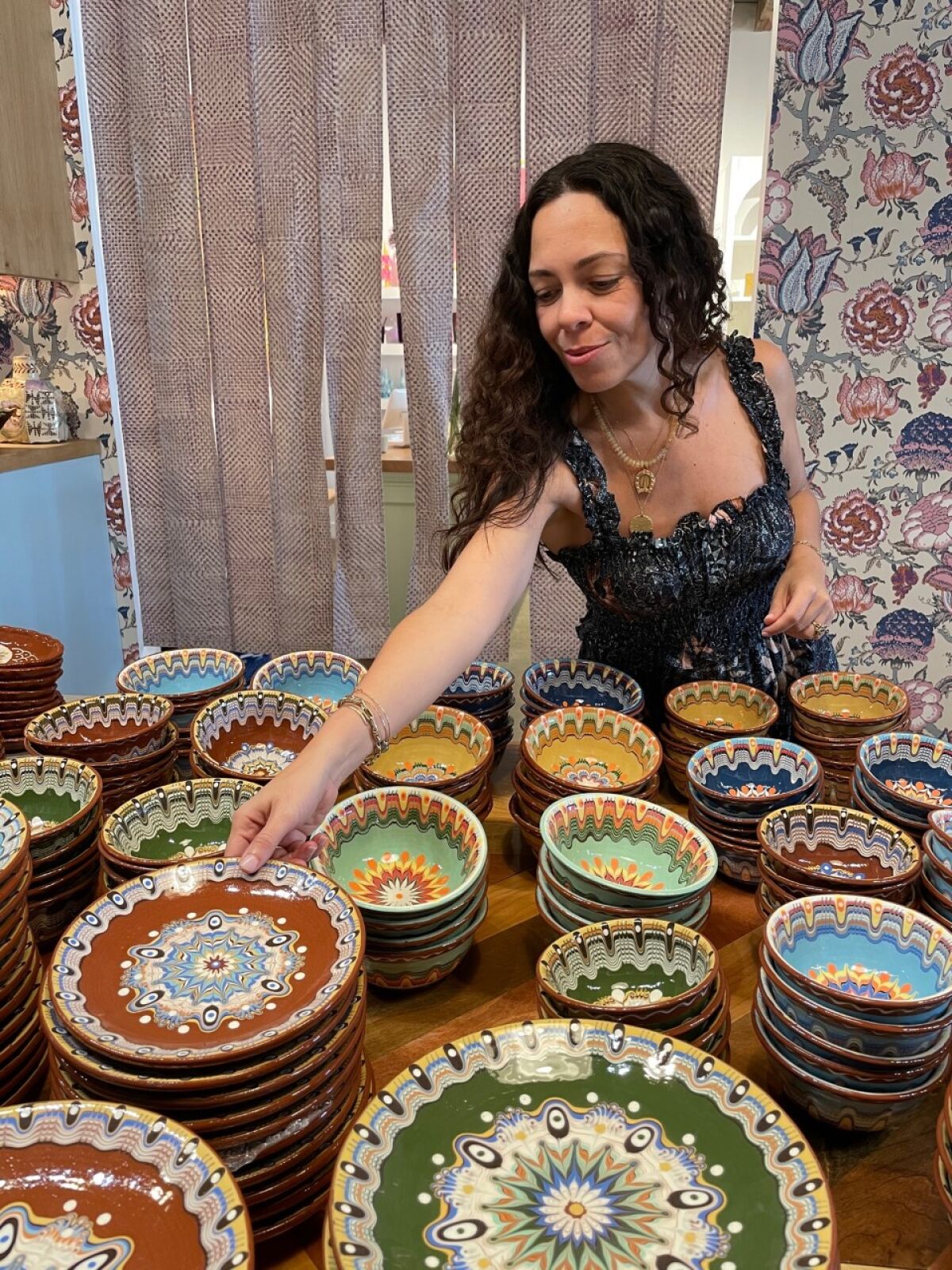 A woman arranges colorful ceramic plates and bowls on a table.