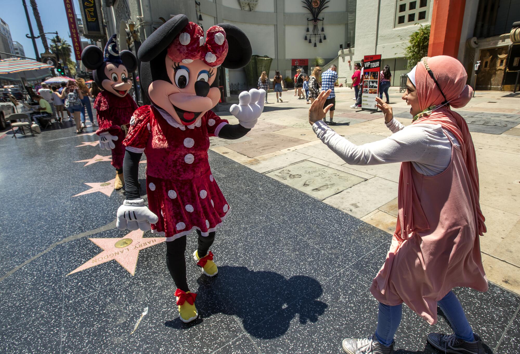 A teenage girl greets a street performer dressed up as Minnie Mouse.