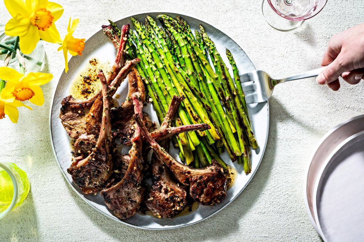 Butter-basted lamb chops are piled on a plate next to bright green asparagus.