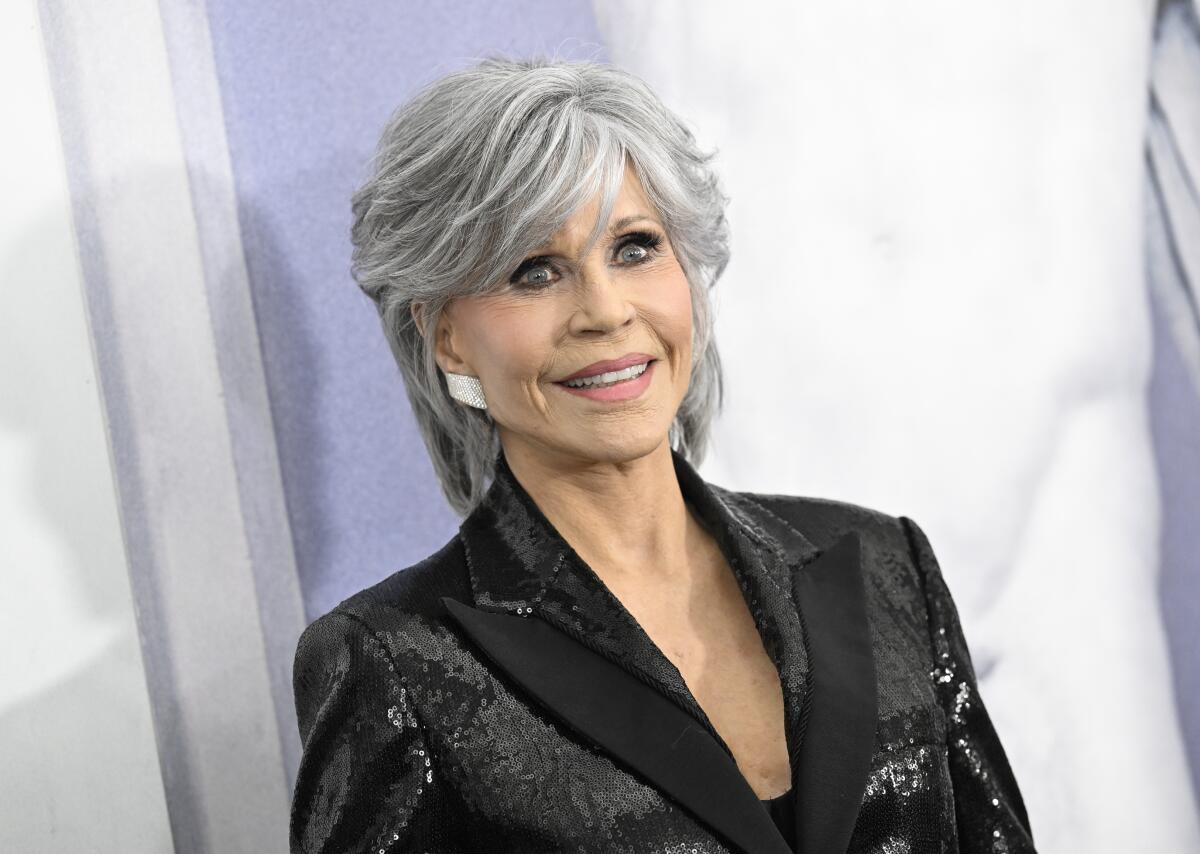 Jane Fonda smiles with silver hair and a black sequin blazer. 