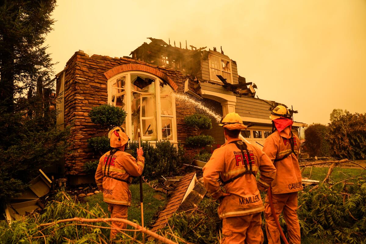 Firefighters douse a burned home amid an orange haze