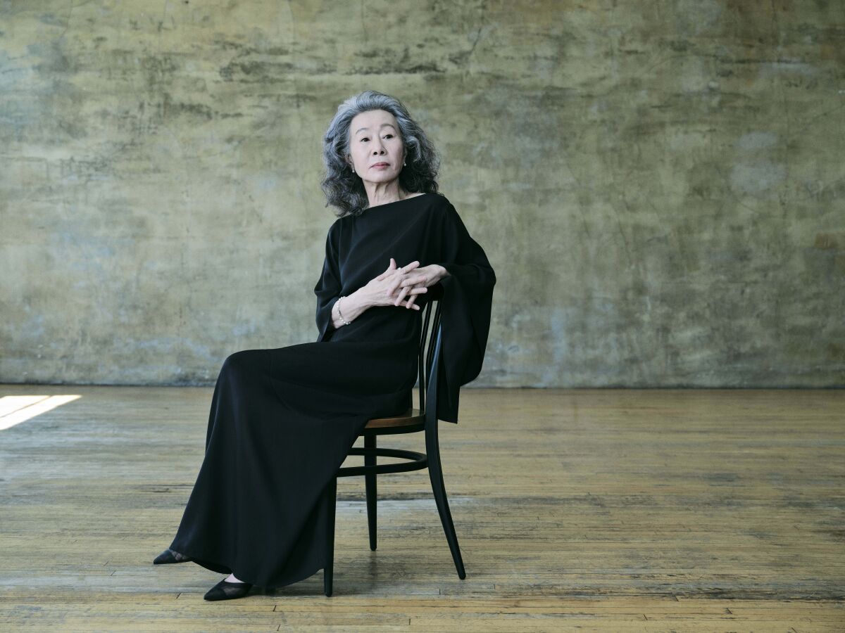 A woman in a black dress sits in a wooden chair for a portrait