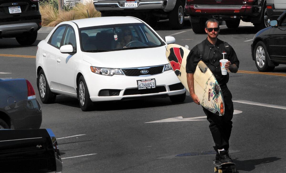 A surfboard-toting skateboarder threads through traffic in Hermosa Beach, where voters will decide whether to loosen a ban on oil and gas drilling.