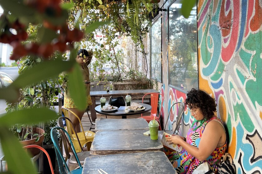 A person sitting at a table in the patio of Yuko Kitchen with a colorful mural on the wall.