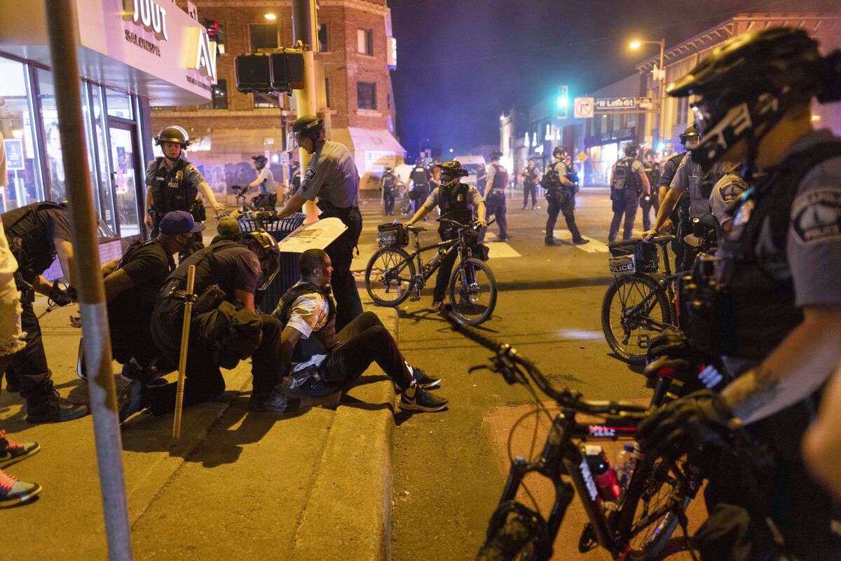 Protesters are detained on a sidewalk surrounded by law enforcement officers