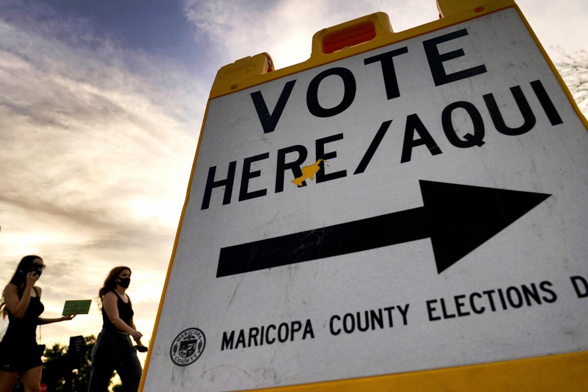 Voters walk beside a sign with an arrow that says, "Vote Here / Aqui"