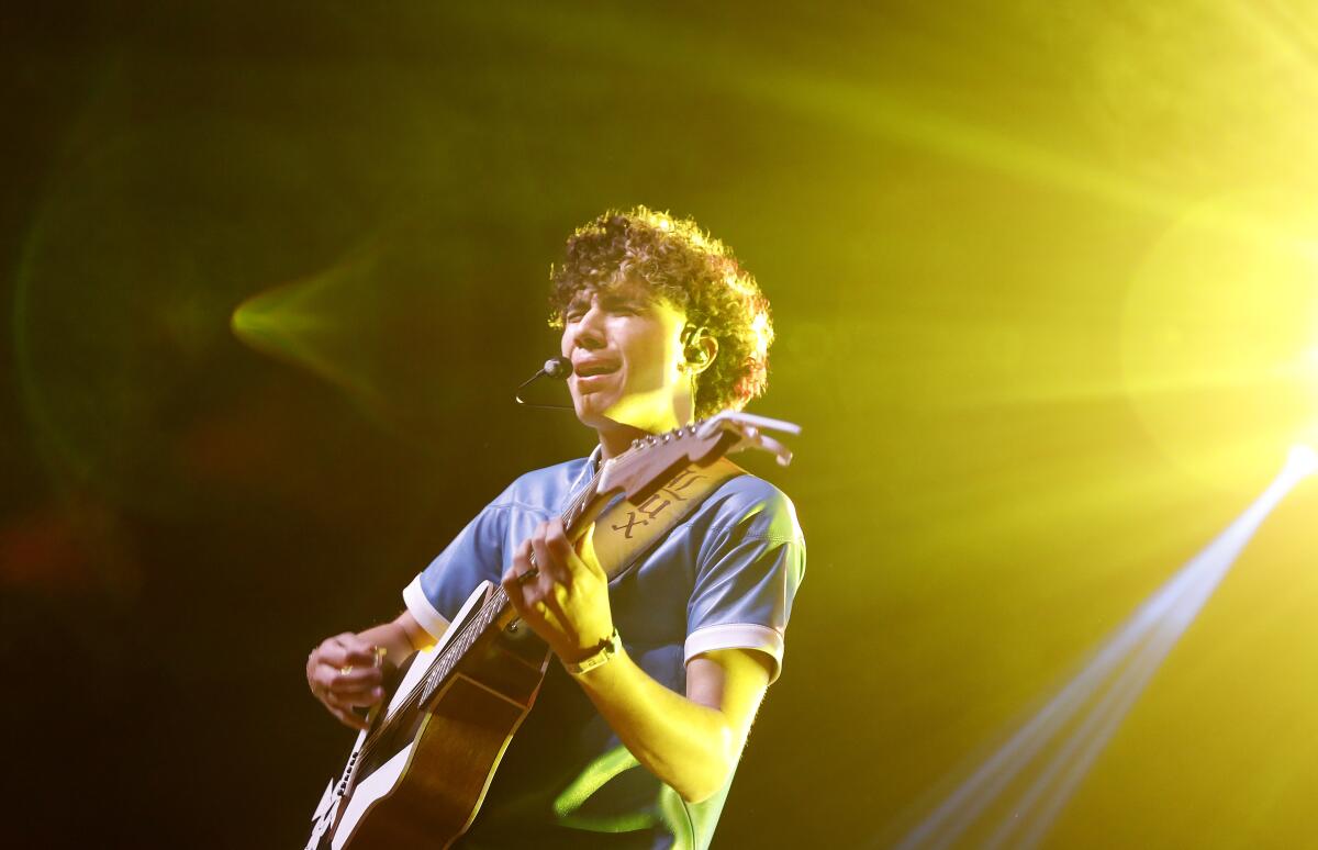 A young singer performs onstage with an acoustic guitar.