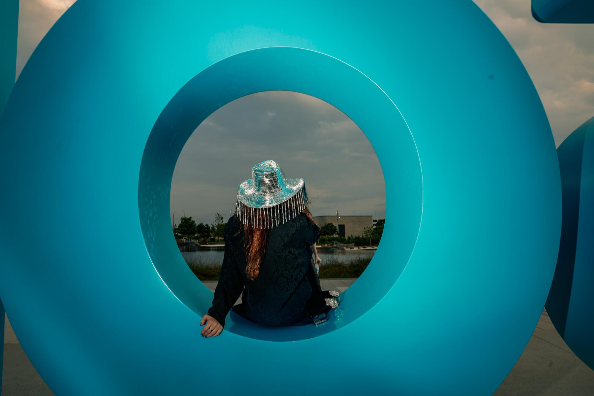 A woman in silver fringed hat poses inside a large blue letter O, part of a sign.