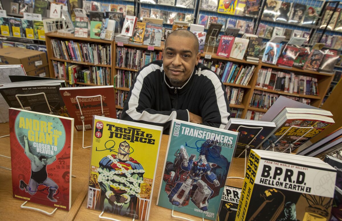 Brandon Easton stands behind a bookcase. Comics atop the case include "Truth & Justice" and "Transformers Galaxies."