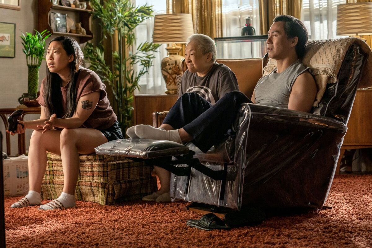 A young woman, an old woman and a middle-aged man in loungewear in their living room, watching TV.