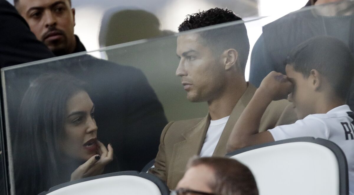 FILE - In this Oct. 2, 2018 file photo, Juventus forward Cristiano Ronaldo, center, is flanked by his girlfriend Georgina, left, and his son Cristiano Jr, as he sits in the stands during a Champions League, group H soccer match between Juventus and Young Boys, at the Allianz stadium in Turin, Italy. Ronaldo's legal fight with a woman who accuses the international soccer star of raping her in his suite at a Las Vegas resort more than 10 years ago is heading toward a court hearing before a federal judge in Las Vegas. (AP Photo/Luca Bruno, File)